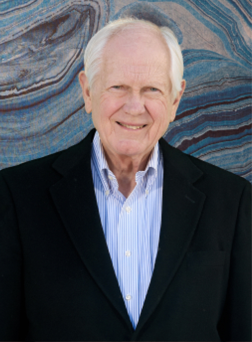 An older man in a black suit jacket and a striped shirt stands in front of a multicolored, swirling abstract background.